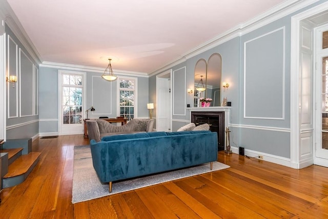 living area with crown molding, a fireplace, a decorative wall, hardwood / wood-style floors, and baseboards