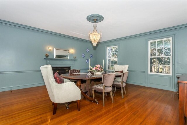 dining room featuring ornamental molding, a decorative wall, wood finished floors, a fireplace, and a notable chandelier
