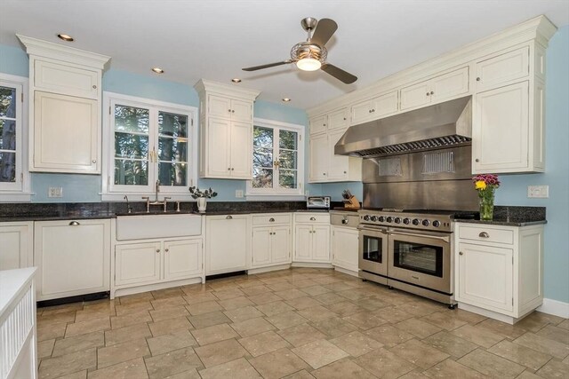 kitchen with exhaust hood, stone finish flooring, double oven range, and a sink