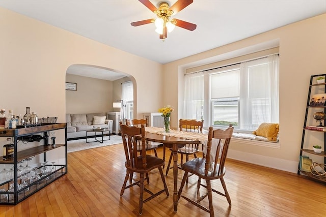 dining area with arched walkways, healthy amount of natural light, light wood finished floors, and ceiling fan