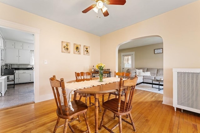 dining room featuring arched walkways, ceiling fan, light wood-style floors, radiator, and baseboards