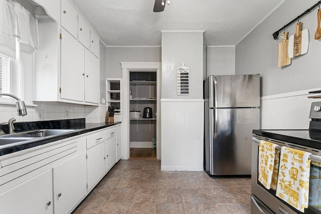 kitchen featuring stainless steel appliances, a sink, white cabinetry, dark countertops, and crown molding