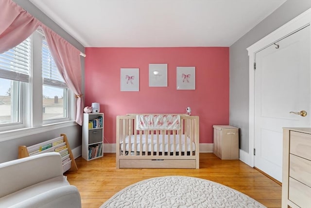 bedroom featuring wood finished floors, a crib, and baseboards