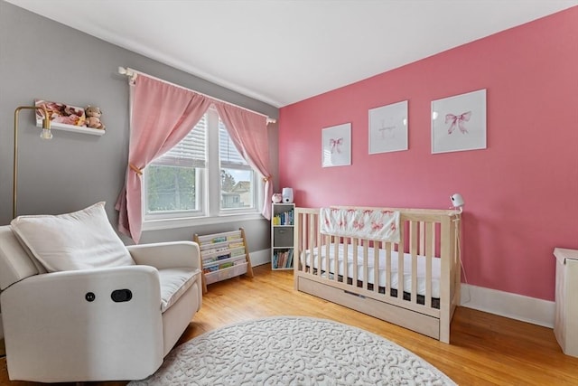 bedroom featuring a crib, wood finished floors, and baseboards