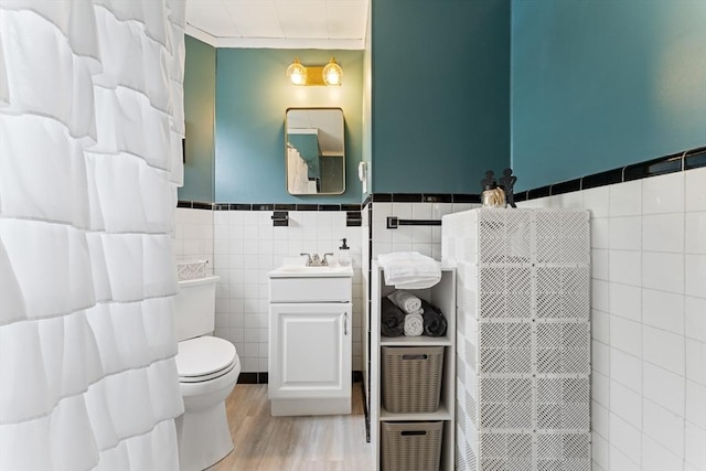 bathroom with tile walls, toilet, vanity, a wainscoted wall, and wood finished floors