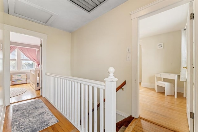 corridor with an upstairs landing, hardwood / wood-style floors, and attic access