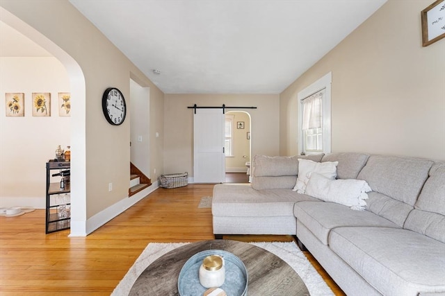 living room with arched walkways, light wood-type flooring, stairs, and baseboards