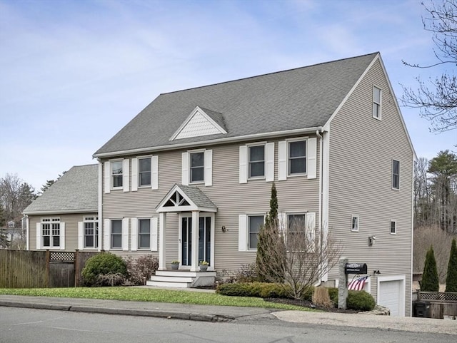 colonial inspired home featuring an attached garage, fence, and roof with shingles
