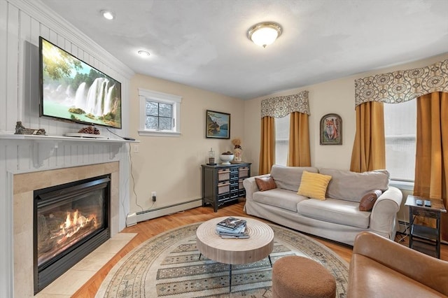 living room with baseboards, a tiled fireplace, baseboard heating, and light wood-style flooring