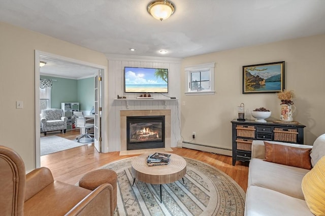 living room featuring a fireplace, a baseboard heating unit, a healthy amount of sunlight, and wood finished floors