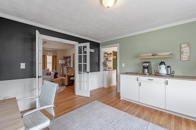 dining area with wainscoting, ornamental molding, french doors, and light wood finished floors