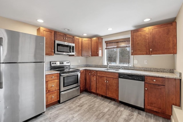 kitchen with a sink, brown cabinetry, light wood-style flooring, stainless steel appliances, and recessed lighting
