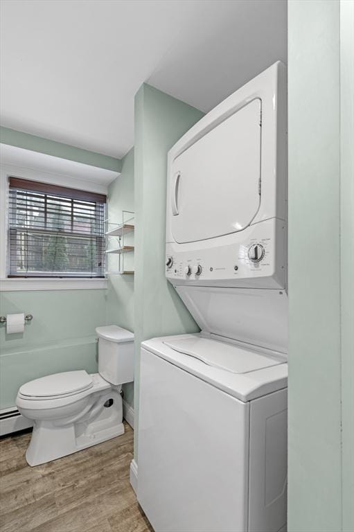 clothes washing area featuring laundry area, baseboards, stacked washer and clothes dryer, and light wood-type flooring