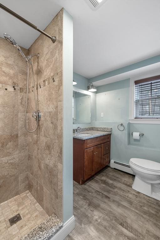 full bath featuring vanity, wood finished floors, toilet, a baseboard heating unit, and a tile shower