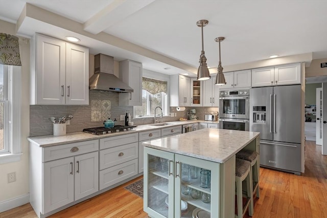 kitchen featuring glass insert cabinets, wall chimney range hood, a sink, backsplash, and stainless steel appliances
