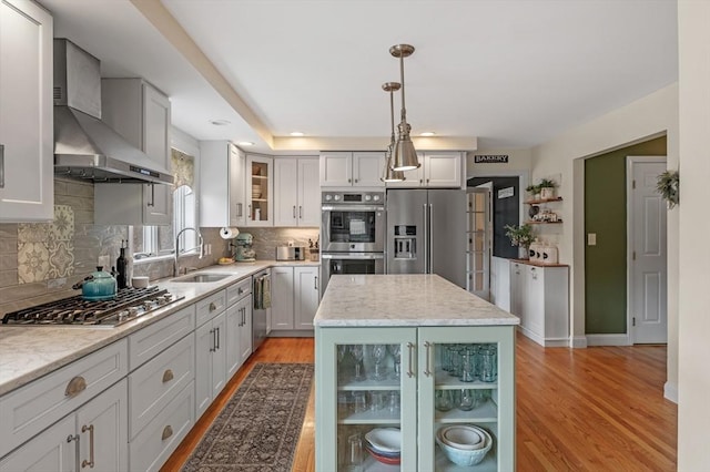kitchen featuring appliances with stainless steel finishes, a sink, light wood-style floors, wall chimney exhaust hood, and tasteful backsplash