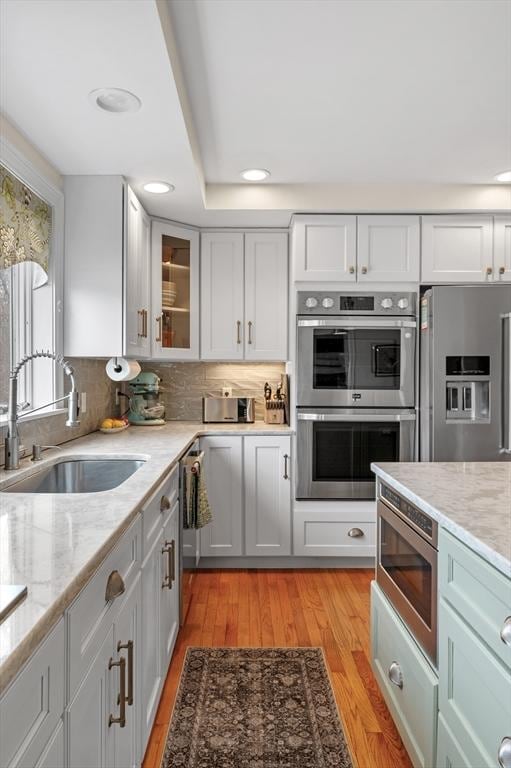 kitchen with appliances with stainless steel finishes, light stone counters, a sink, light wood-style flooring, and recessed lighting
