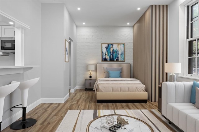 bedroom with an accent wall, baseboards, wood finished floors, and recessed lighting