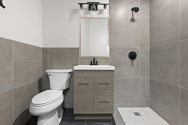 bathroom with toilet, a tile shower, tile walls, and vanity