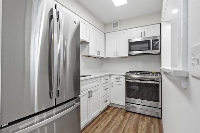 kitchen featuring stainless steel appliances, visible vents, white cabinetry, light countertops, and light wood-type flooring