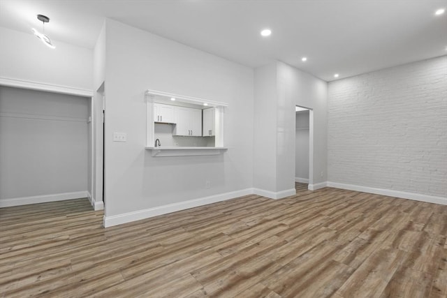 unfurnished living room with recessed lighting, baseboards, brick wall, and wood finished floors