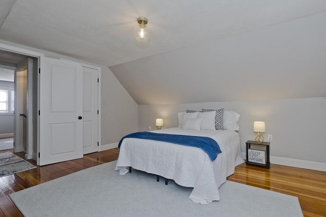 bedroom with lofted ceiling, wood-type flooring, and baseboards