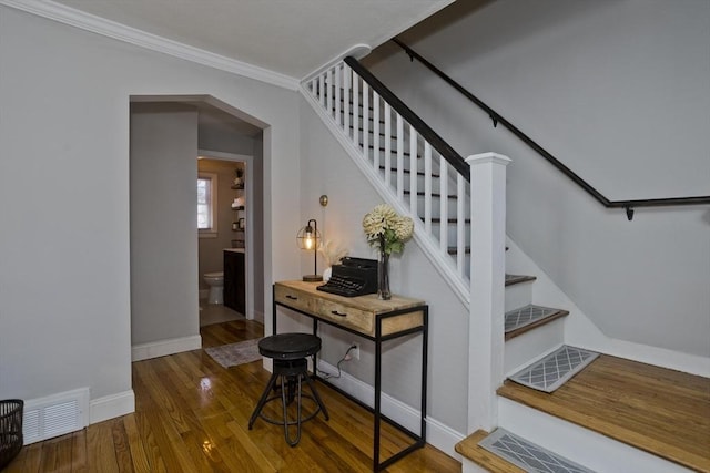 stairs with arched walkways, wood finished floors, visible vents, baseboards, and ornamental molding