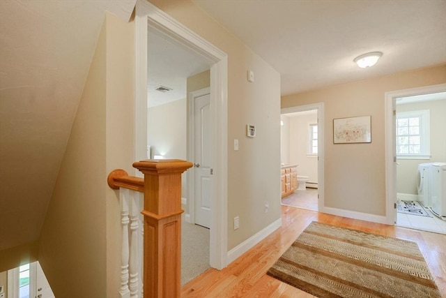 corridor featuring baseboards, visible vents, washing machine and dryer, and light wood finished floors
