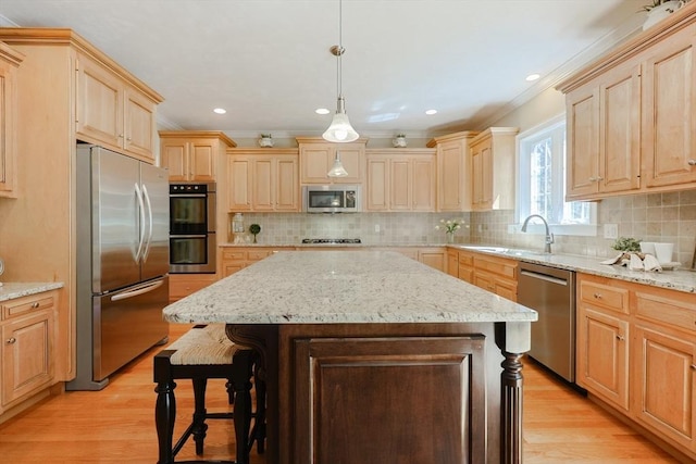 kitchen with appliances with stainless steel finishes, a sink, light brown cabinets, light wood-type flooring, and a kitchen island