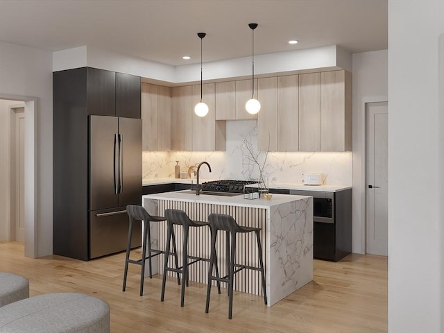 kitchen featuring pendant lighting, light hardwood / wood-style floors, stainless steel refrigerator, and a center island with sink