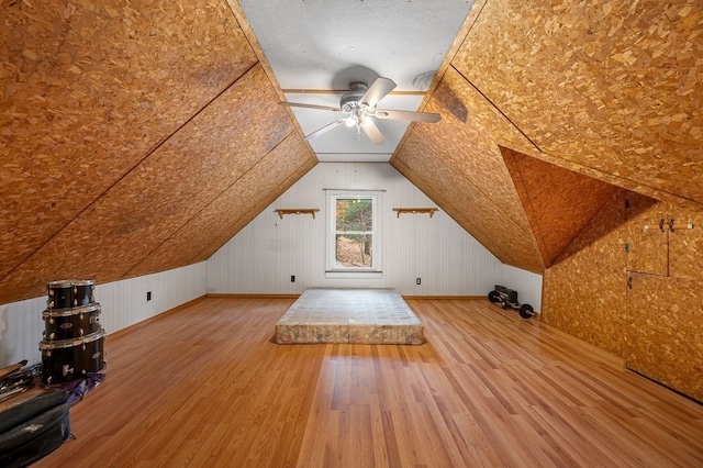 additional living space featuring lofted ceiling, ceiling fan, wood walls, and hardwood / wood-style flooring