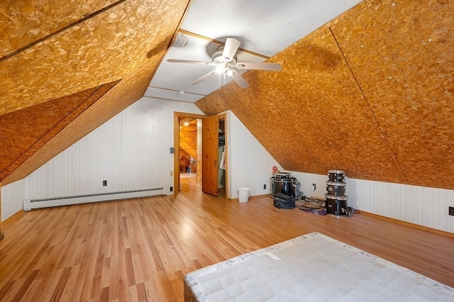 additional living space featuring ceiling fan, a baseboard radiator, wood walls, vaulted ceiling, and hardwood / wood-style flooring