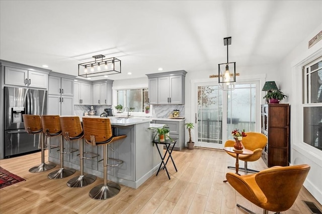 kitchen featuring visible vents, stainless steel fridge with ice dispenser, a kitchen island, gray cabinets, and light countertops