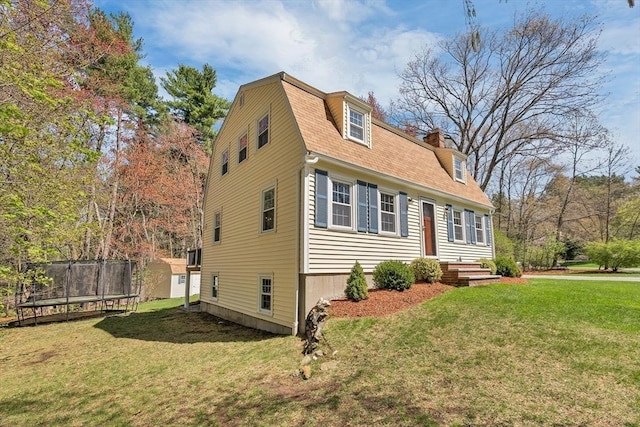 view of side of property featuring roof with shingles, a trampoline, a chimney, and a yard
