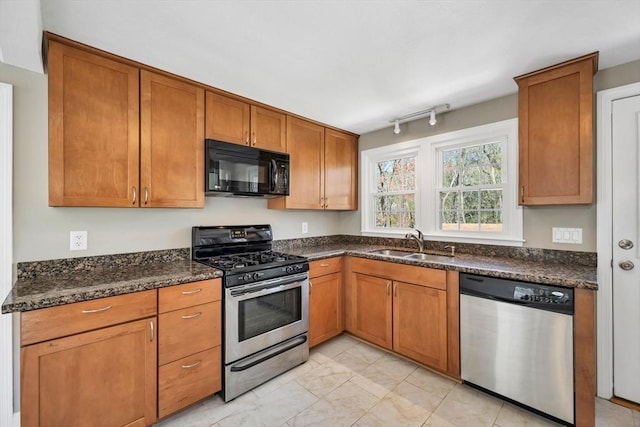 kitchen featuring brown cabinetry, a sink, dark stone countertops, and stainless steel appliances
