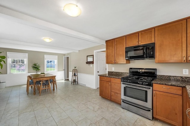 kitchen featuring black microwave, gas stove, brown cabinetry, and dark stone counters