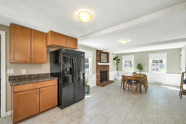 kitchen featuring brown cabinetry, visible vents, black refrigerator with ice dispenser, a fireplace, and dark stone counters