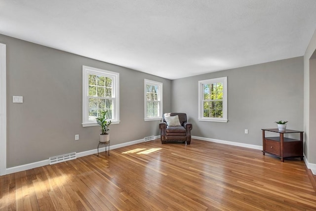 living area featuring baseboards, plenty of natural light, light wood-style flooring, and visible vents