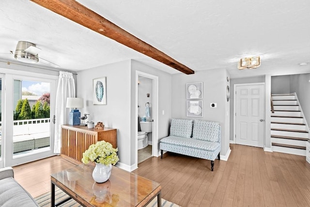 living area featuring stairway, wood finished floors, baseboards, beam ceiling, and a chandelier