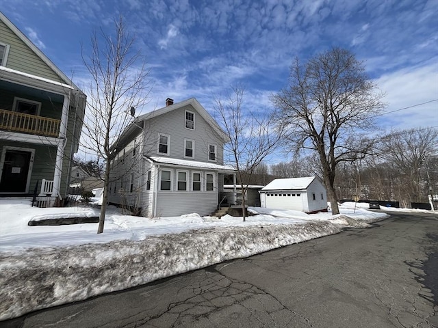 snow covered property with a garage, a chimney, and an outbuilding