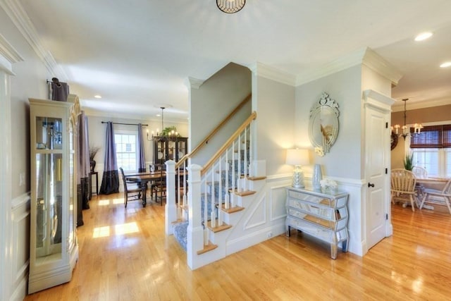 staircase with an inviting chandelier, plenty of natural light, and ornamental molding