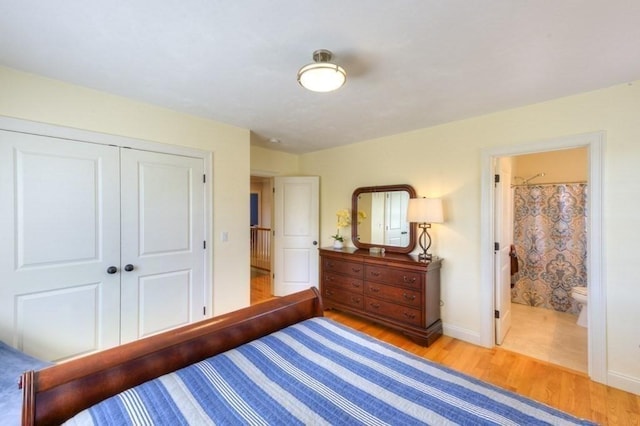 bedroom with baseboards, ensuite bath, wood finished floors, and a closet