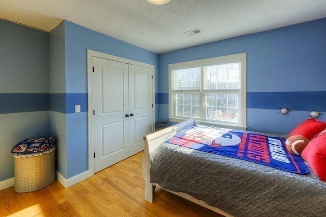 bedroom with baseboards, a closet, wood finished floors, and visible vents