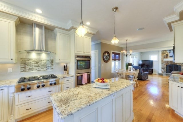 kitchen featuring a kitchen island, crown molding, open floor plan, stainless steel appliances, and wall chimney exhaust hood