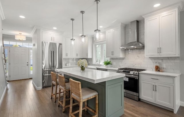 kitchen featuring wall chimney exhaust hood, a kitchen island, white cabinetry, and appliances with stainless steel finishes