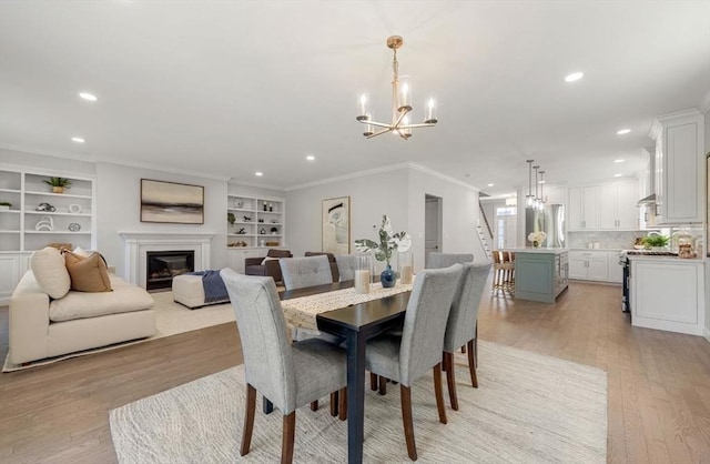 dining area with a chandelier, built in shelves, light hardwood / wood-style floors, and crown molding