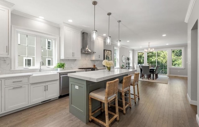 kitchen with stainless steel dishwasher, sink, wall chimney range hood, white cabinets, and a kitchen island