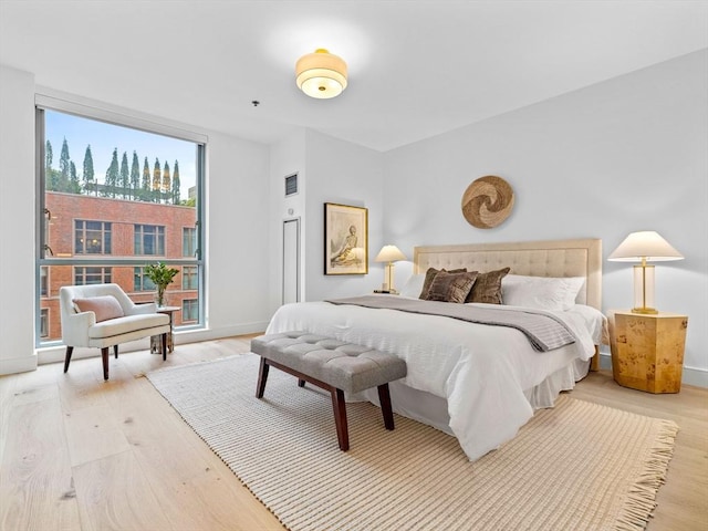 bedroom featuring light wood finished floors, floor to ceiling windows, and baseboards