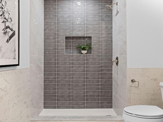 bathroom featuring wainscoting, tiled shower, toilet, and tile walls