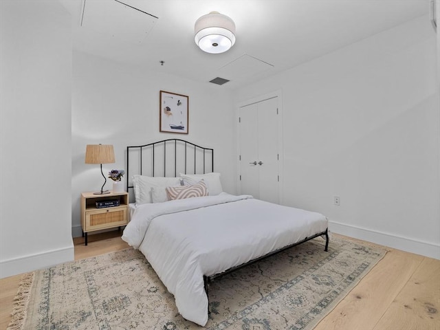 bedroom featuring visible vents, baseboards, attic access, and wood finished floors